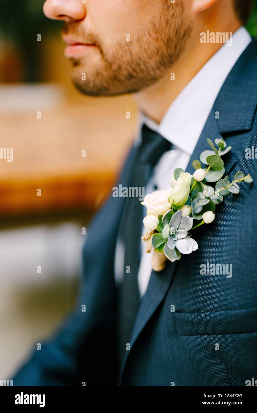 Un uomo non rasato in una giacca blu, camicia bianca, cravatta e con un boutonniere di rose ed echeveria Foto Stock