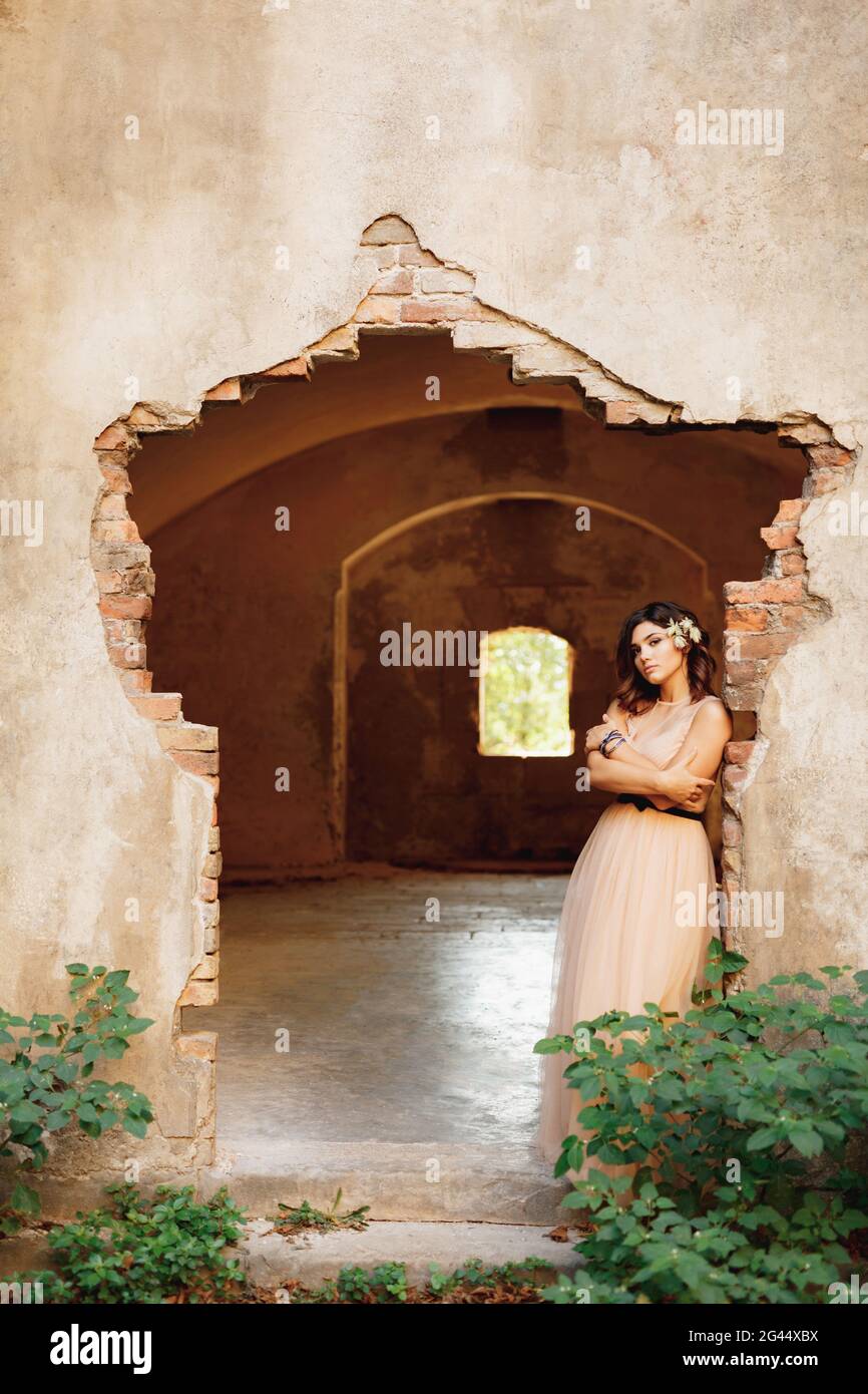 Bella sposa in un bel vestito pastello con le braccia attraversata sul petto si trova in piedi penosamente sulle rovine di un castello Foto Stock