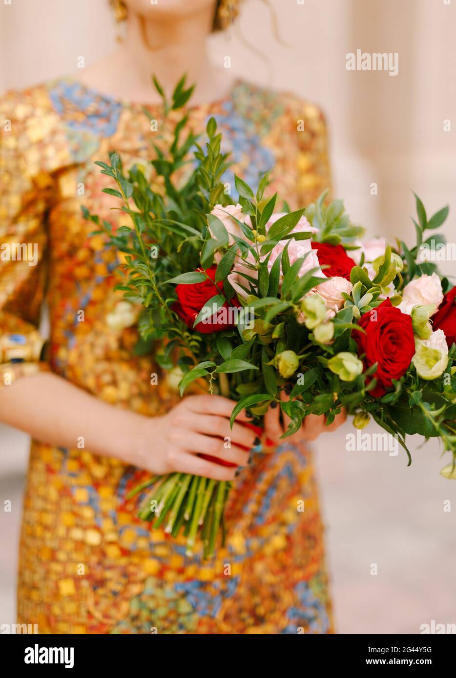 Una sposa in un abito d'oro insolito tiene un bouquet nuziale di rose bianche e rosse nelle sue mani, primo piano Foto Stock