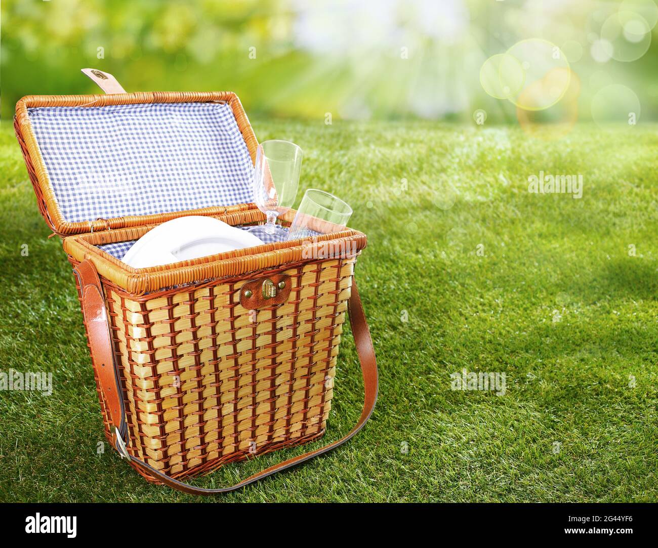 Sfondo estivo e primaverile con cesto di vimini aperto con accessori da picnic posto su prato verde erboso in giornata di sole con effetto sfocato Foto Stock