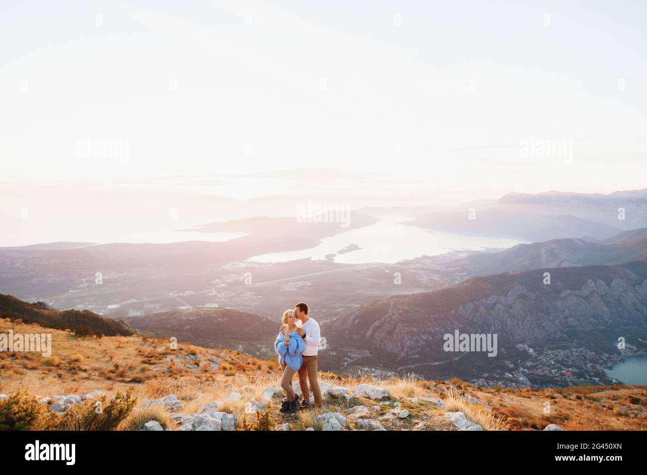 L'uomo abbraccia una donna in un maglione blu sulle spalle sullo sfondo del Monte Lovcen, baia di Kotor, Montenegro Foto Stock
