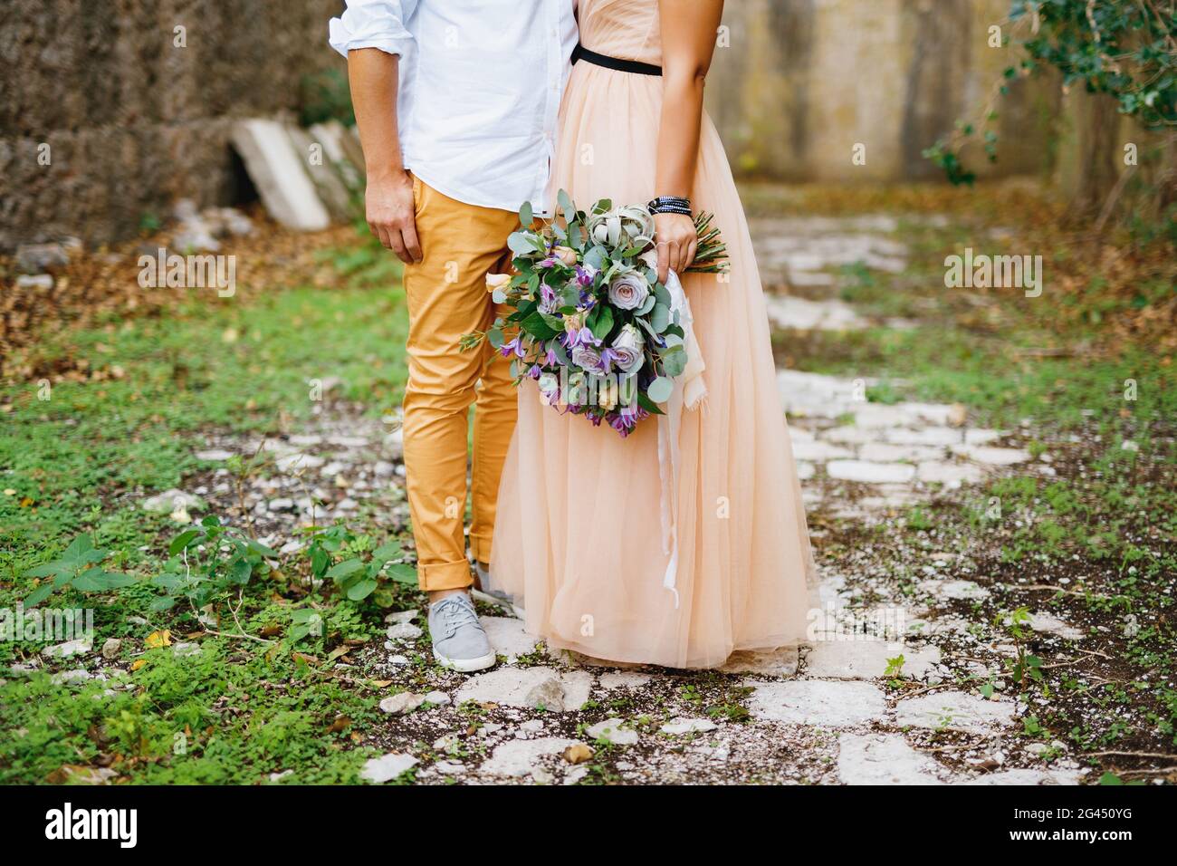 Mezzo-ritratto di sposo abbracciando sposa in un bel vestito con un bouquet nelle sue mani sullo sfondo di a. muro di pietra Foto Stock