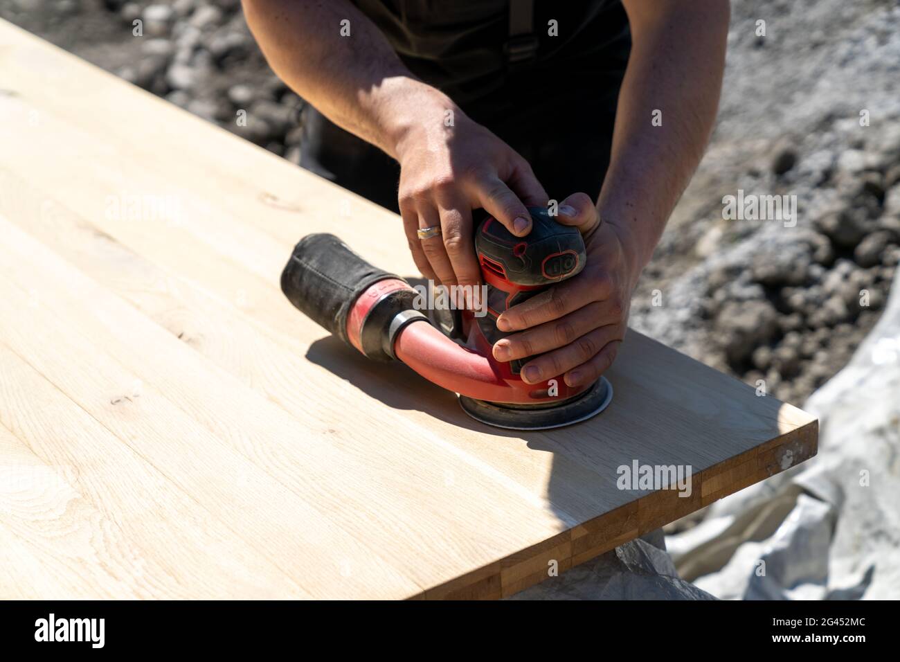 Lavoratori edili che utilizzano una smerigliatrice elettrica senza fili per carteggiare un enorme piano da tavolo in legno Foto Stock