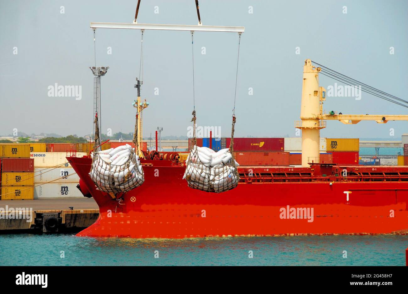 Nel porto di Lomé, Togo, una gru sta scaricando merci da una nave, mentre un'altra nave è attraccata accanto ad un molo dei container, in un giorno tropicale, cielo blu. Foto Stock