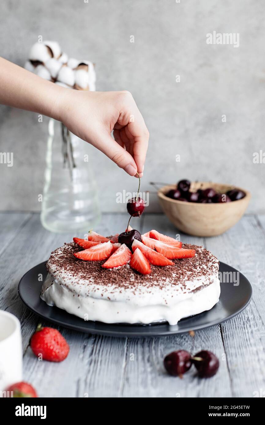 Dolce torta di frutti di bosco decorata con ciliegie e fragole, ricoperta di panna bianca. Dolce cibo ancora vita. Foto Stock