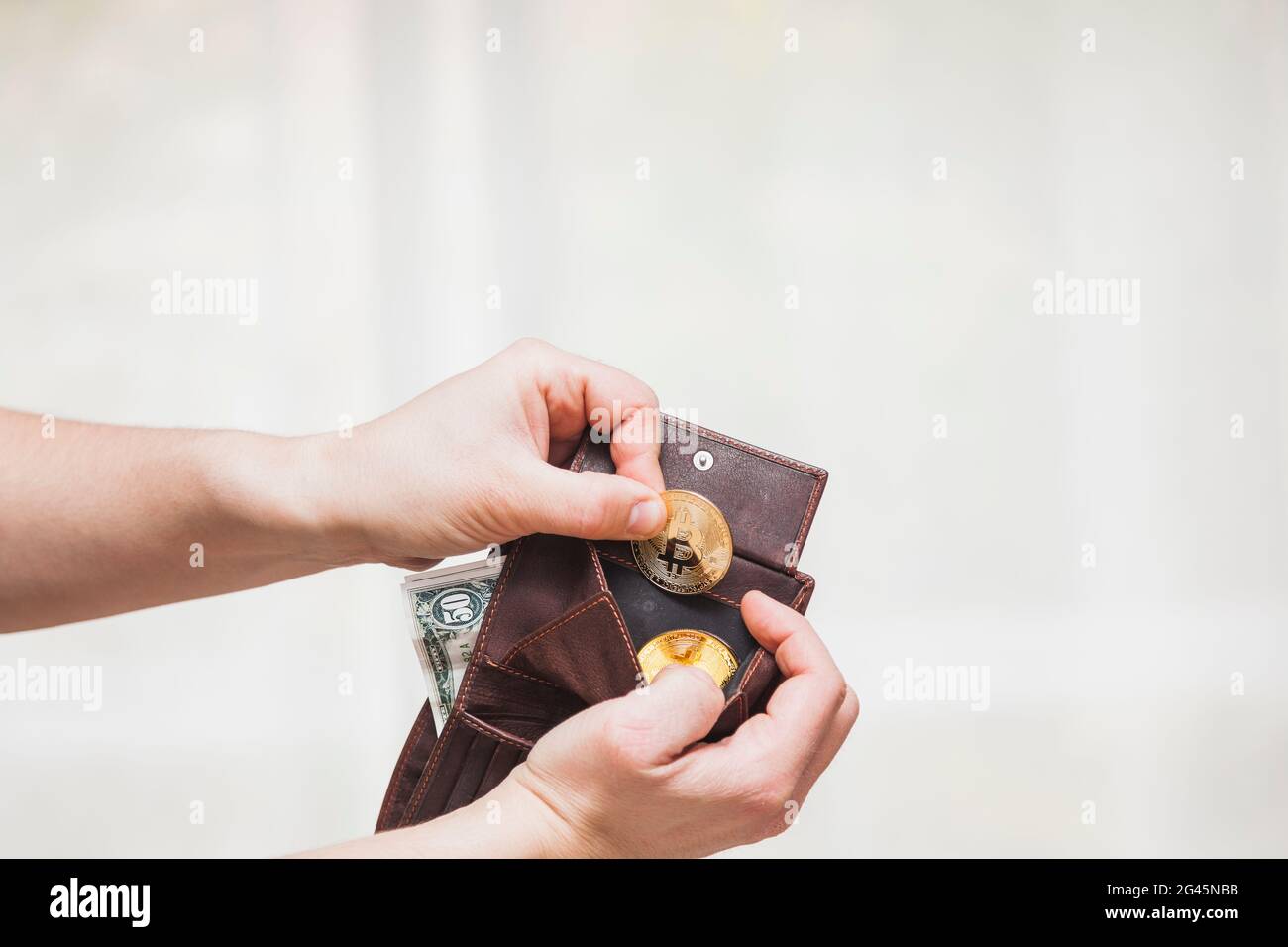 Le mani di un uomo rimuovono le criptovalute dalla borsa di un portafoglio di pelle marrone in cui ci sono anche le fatture del dollaro. Foto Stock