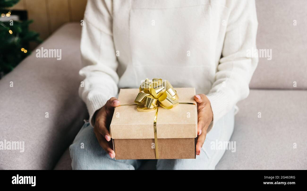 Le mani africane della donna tengono natale o nuovo anno nastro d'oro decorato scatola regalo. Foto Stock