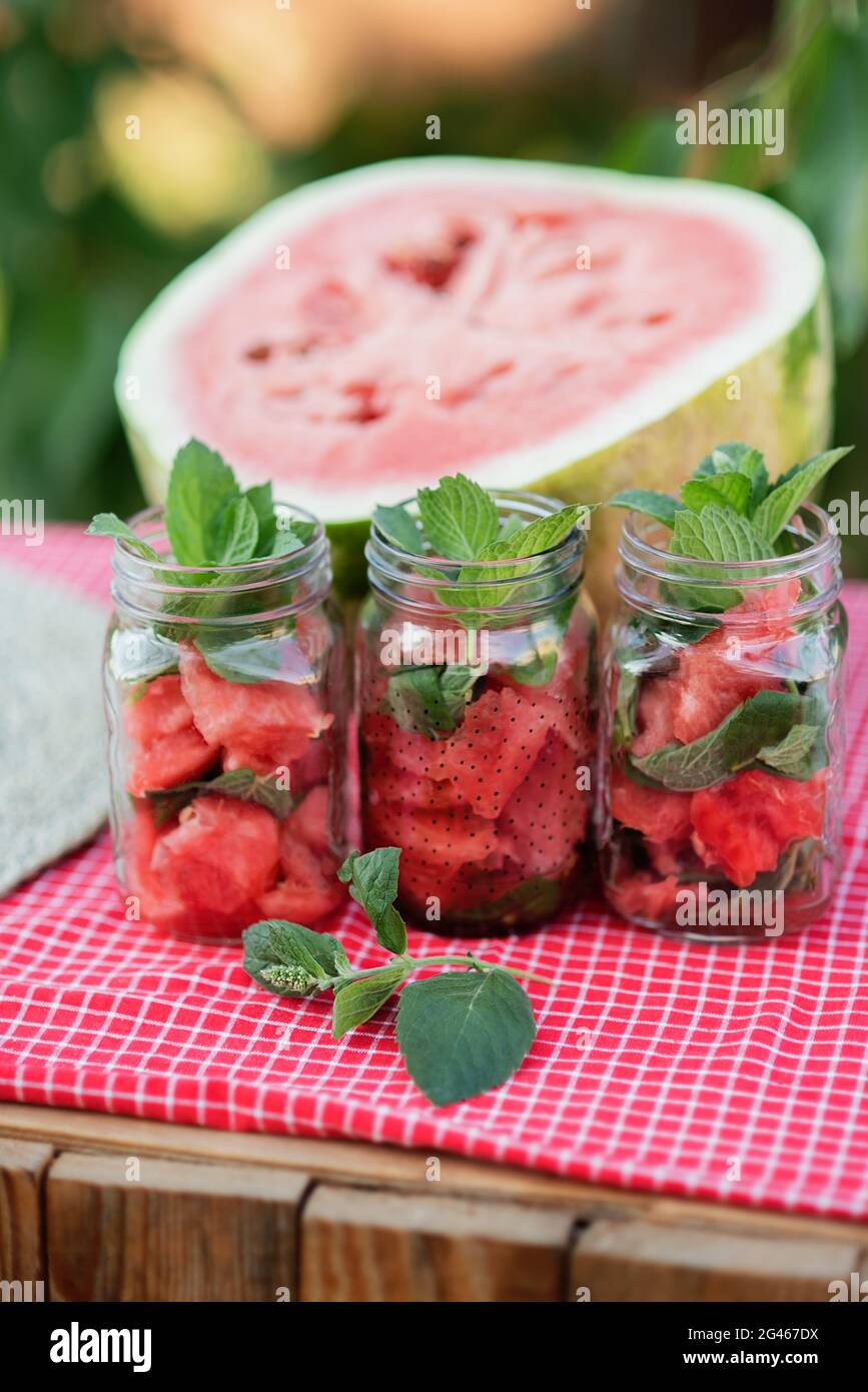 Anguria e menta infusarono acqua detox. Limonata con ghiaccio e menta come rinfrescante bevanda estiva in vasi. Bevande analcoliche fredde con frutta. Rinfrescante su rosso Foto Stock