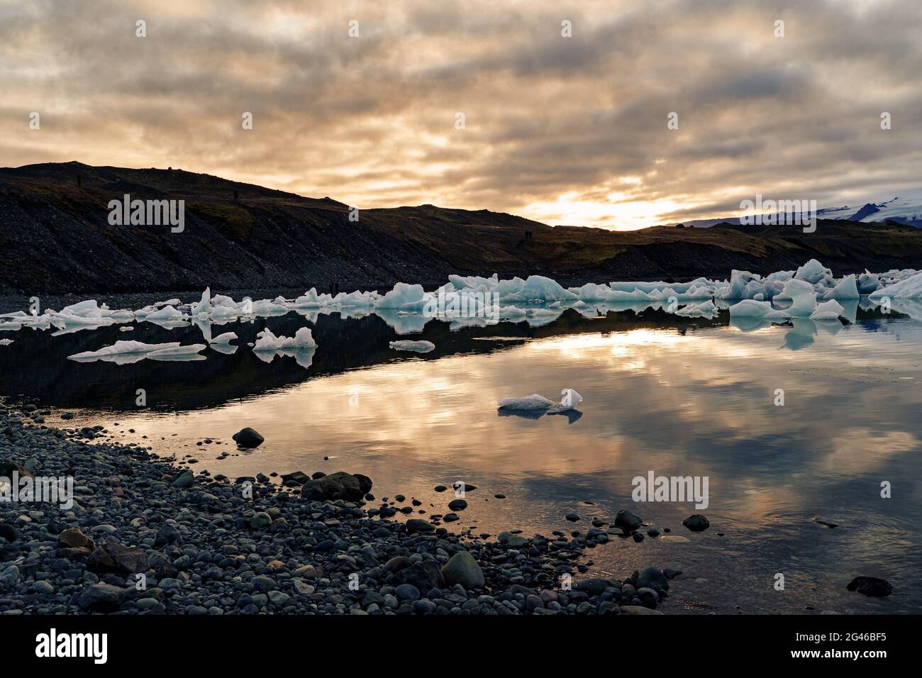 Gli iceberg si allontanano nella laguna al tramonto mentre il sole tramonta dietro la catena montuosa. Jokulsarlon, Islanda Foto Stock