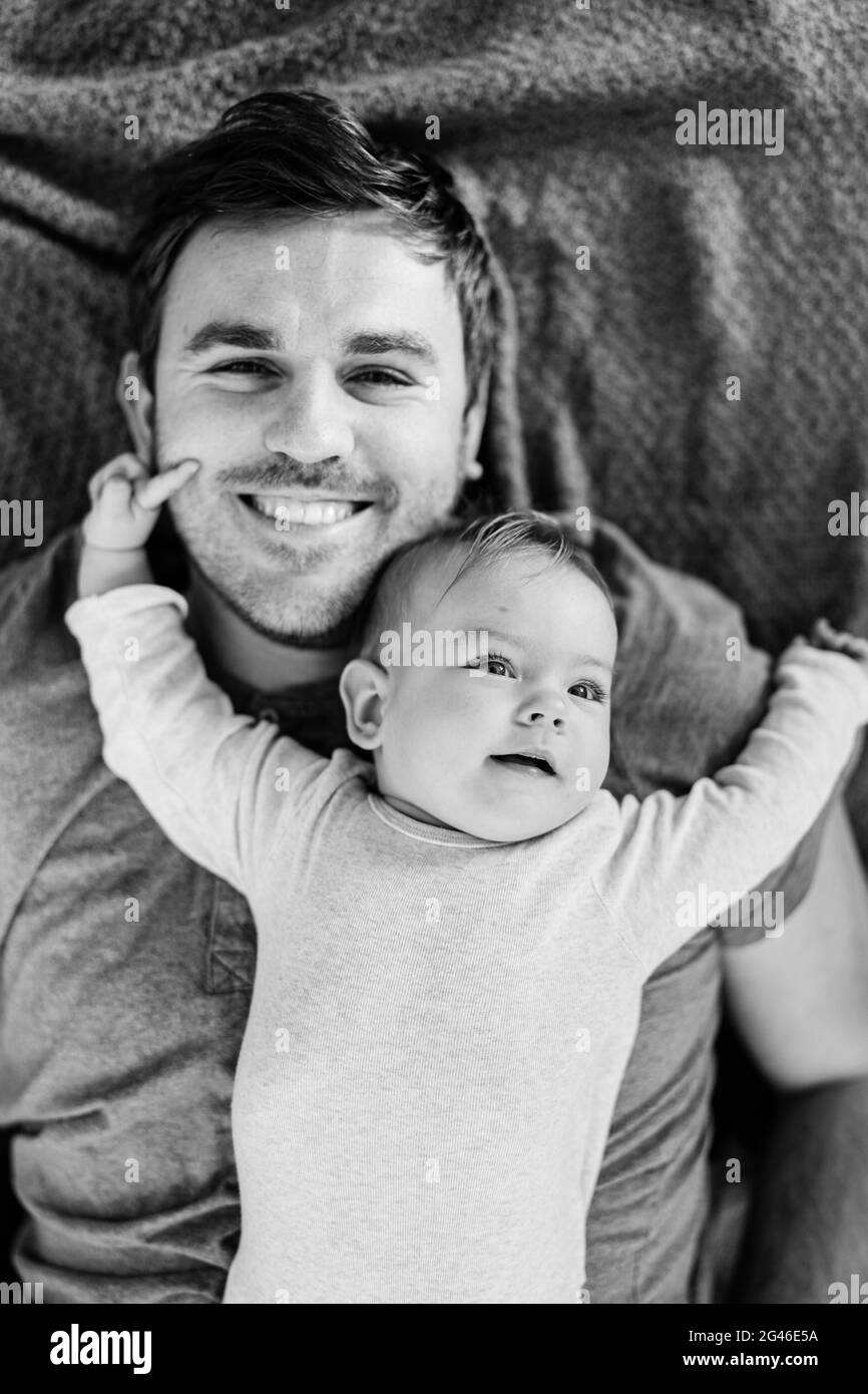 Il piccolo bambino si trova con la schiena sul petto di un papà sorridente, braccia allungate. Foto in bianco e nero. Primo piano Foto Stock
