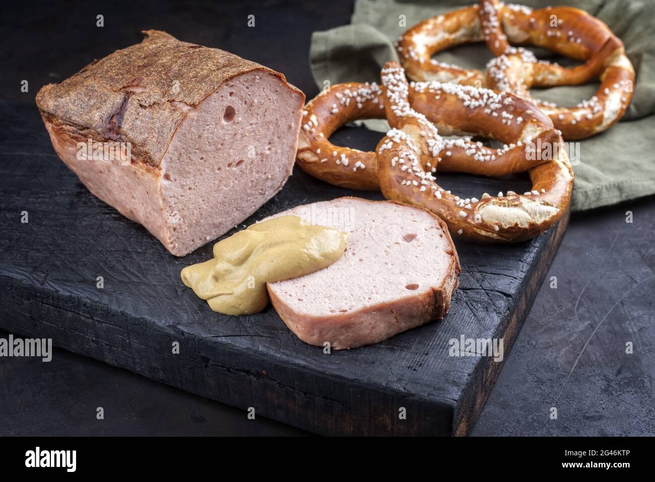 Tradizionale leberkaese bavarese fresco al forno a fette e come pezzo servito con pretzel e senape calda come primo piano su un vecchio rustico Foto Stock