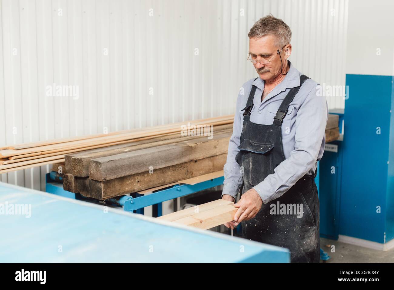 Ritratto di un falegname o falegname anziano che lavora con tavole di legno in un laboratorio di falegname. Foto Stock