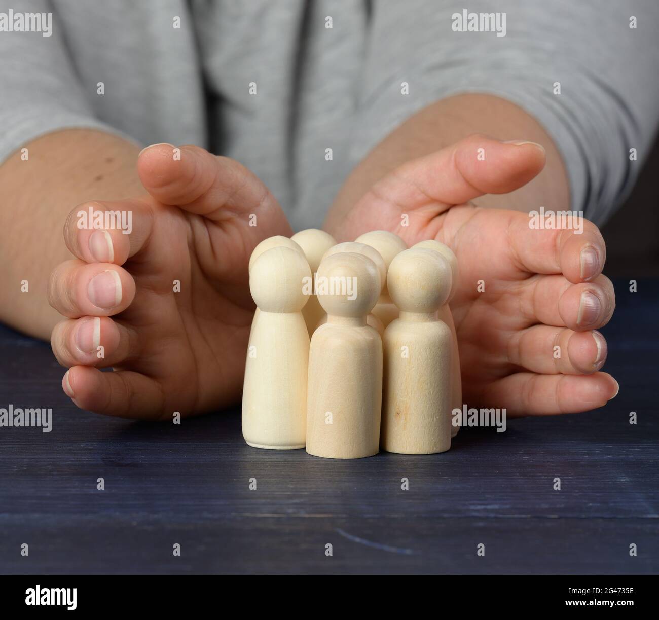 Le mani femminili proteggono le figure di legno degli uomini. Concetto di protezione e mentoring. Preservazione della squadra in tempi di crisi Foto Stock