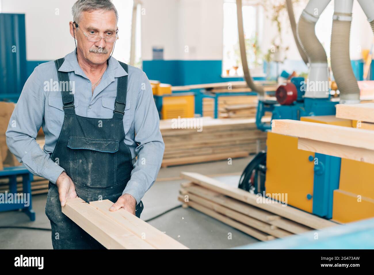 Ritratto di un falegname o falegname anziano che lavora con tavole di legno in un laboratorio di falegname. Foto Stock