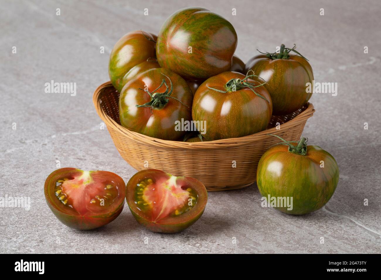 Cestino con pomodori maturi rossi e verdi a strisce intere e pomodori freschi a metà da vicino Foto Stock