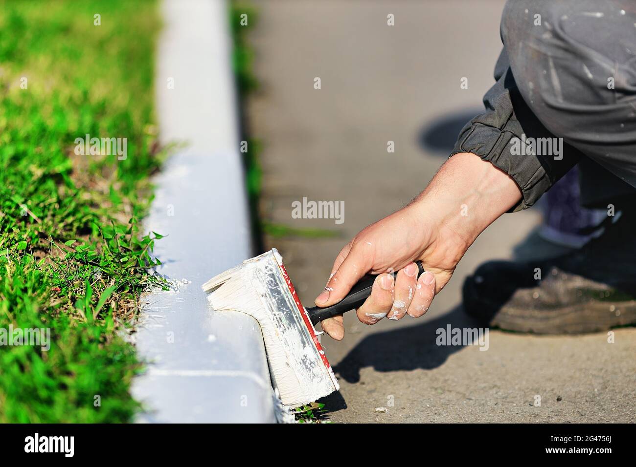 Un lavoratore in tute dipinge un bordo con vernice bianca in una giornata estiva. Servizi urbani, architettura paesaggistica. Foto Stock