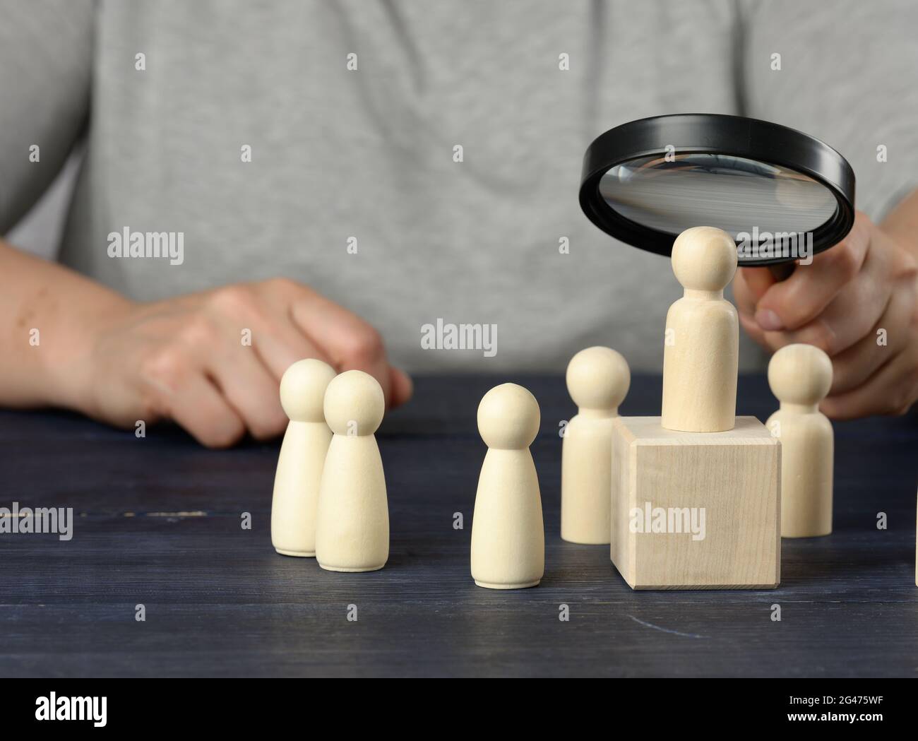 Una mano con una lente d'ingrandimento esamina uomini di legno unici e di talento nella folla Foto Stock