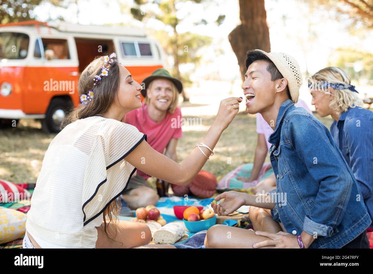 Donna che alimenta la frutta ad un amico mentre si siede sul campo Foto Stock