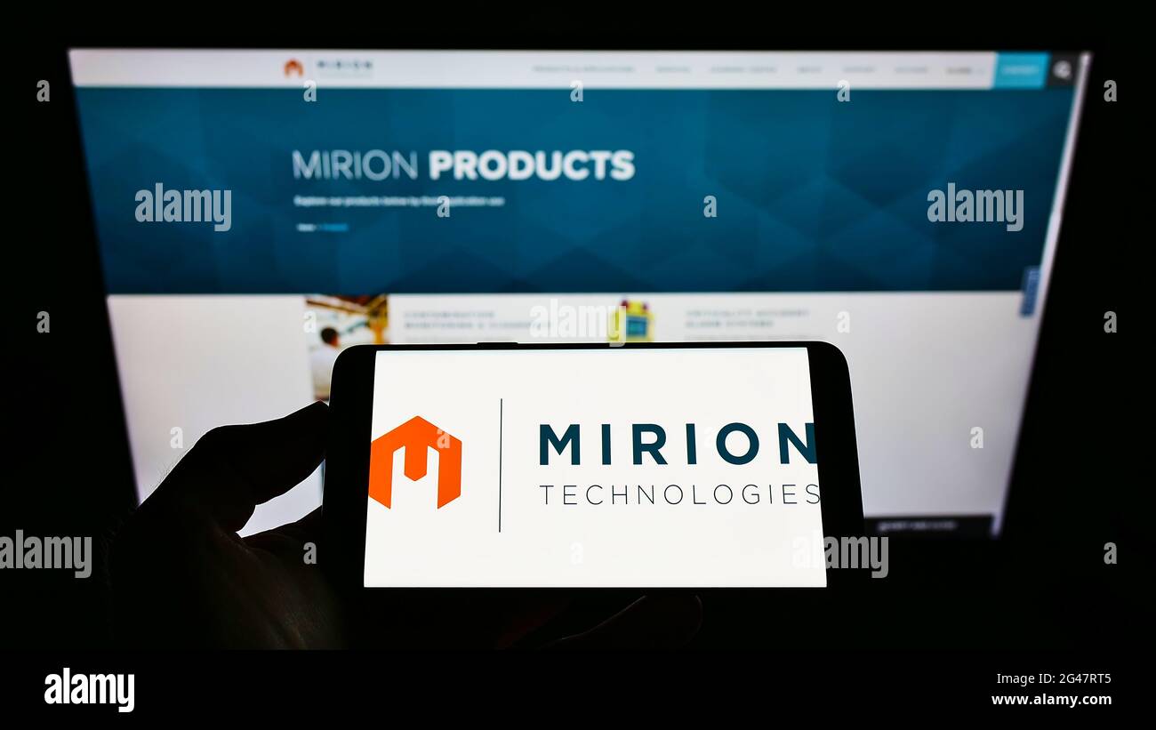 Persona che tiene il telefono mobile con il logo della società di decadimento radioattivo Mirion Technologies Inc. Sullo schermo davanti alla pagina web. Mettere a fuoco il display del telefono. Foto Stock
