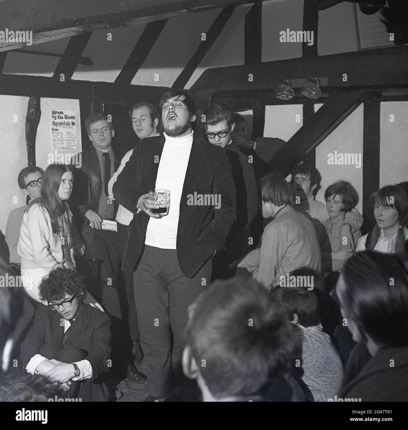 1970, musica storica, folk, all'interno di una stanza in un pub di campagna con travi di legno, un pubblico che ascolta un cantante folk maschile bearded cantare una canzone al Castle Inn, Colchester, Essex, Inghilterra, Regno Unito. Foto Stock