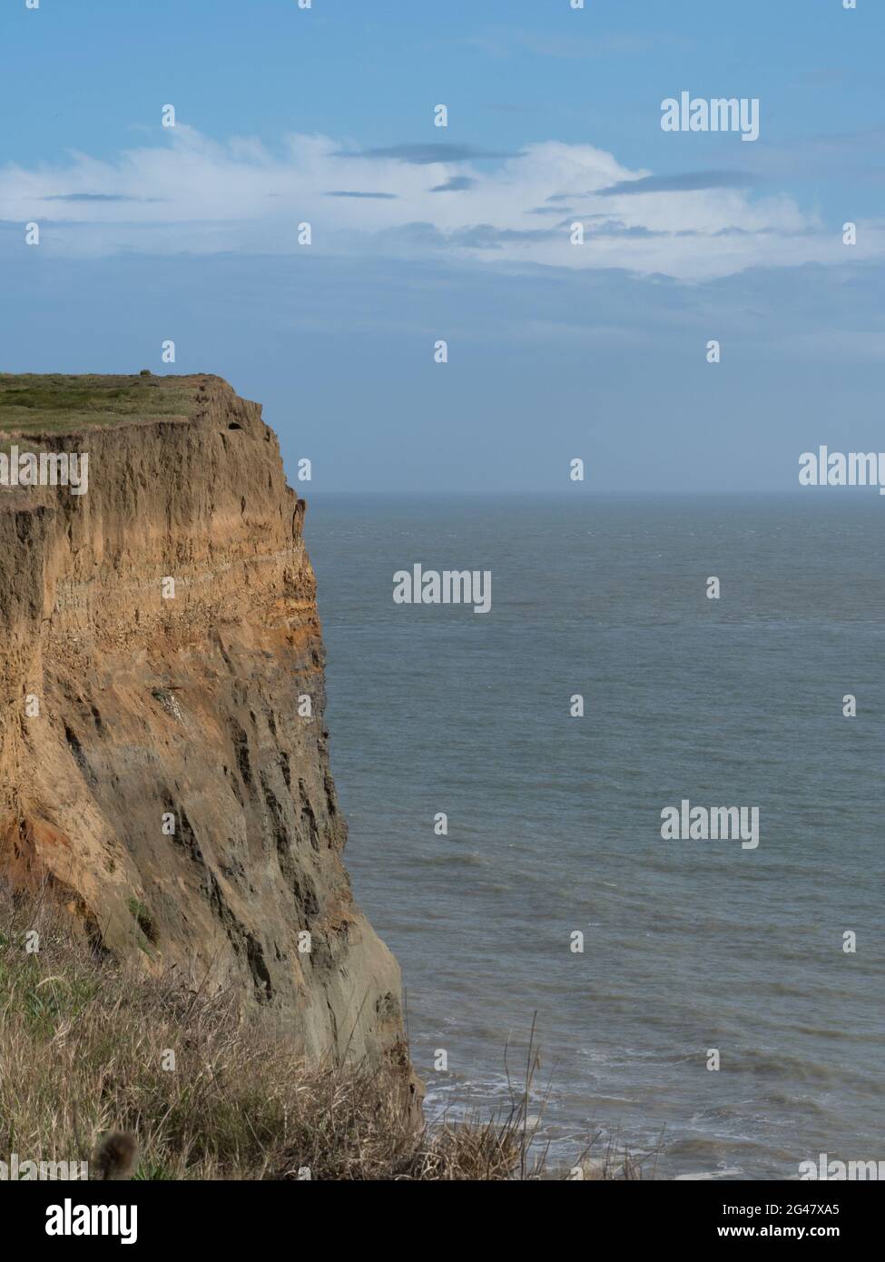 Scogliera a strati sotto un piccolo strato di nuvole attraenti in cielo blu sopra il calmo mare dell'oceano Atlantico Foto Stock