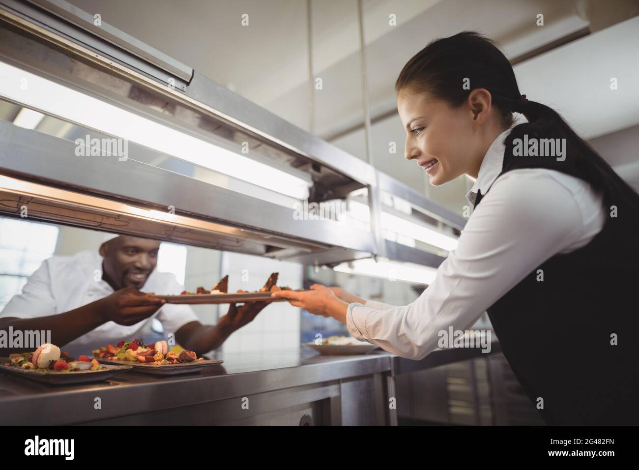 Lo chef consegna il piatto alimentare alla cameriera alla stazione d'ordine Foto Stock