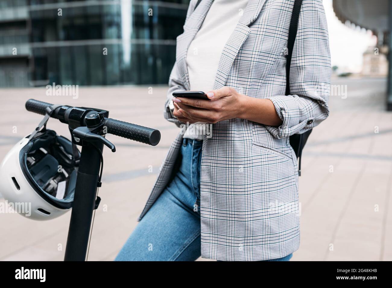 Scatto corto di femmina in casuals usando un'applicazione su un telefono cellulare per sbloccare lo scooter elettrico a spinta Foto Stock