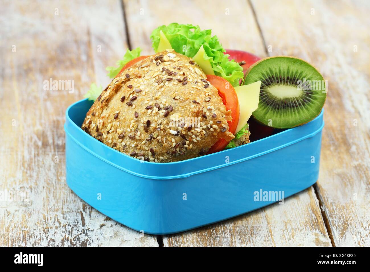 Scatola per il pranzo sana contenente un rotolo di formaggio a grani interi con lattuga, pomodoro e kiwi Foto Stock
