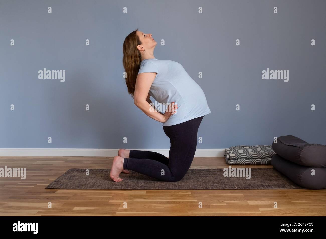 Donna in gravidanza sana di lunghezza intera che fa yoga che si esercita stretching a casa Foto Stock