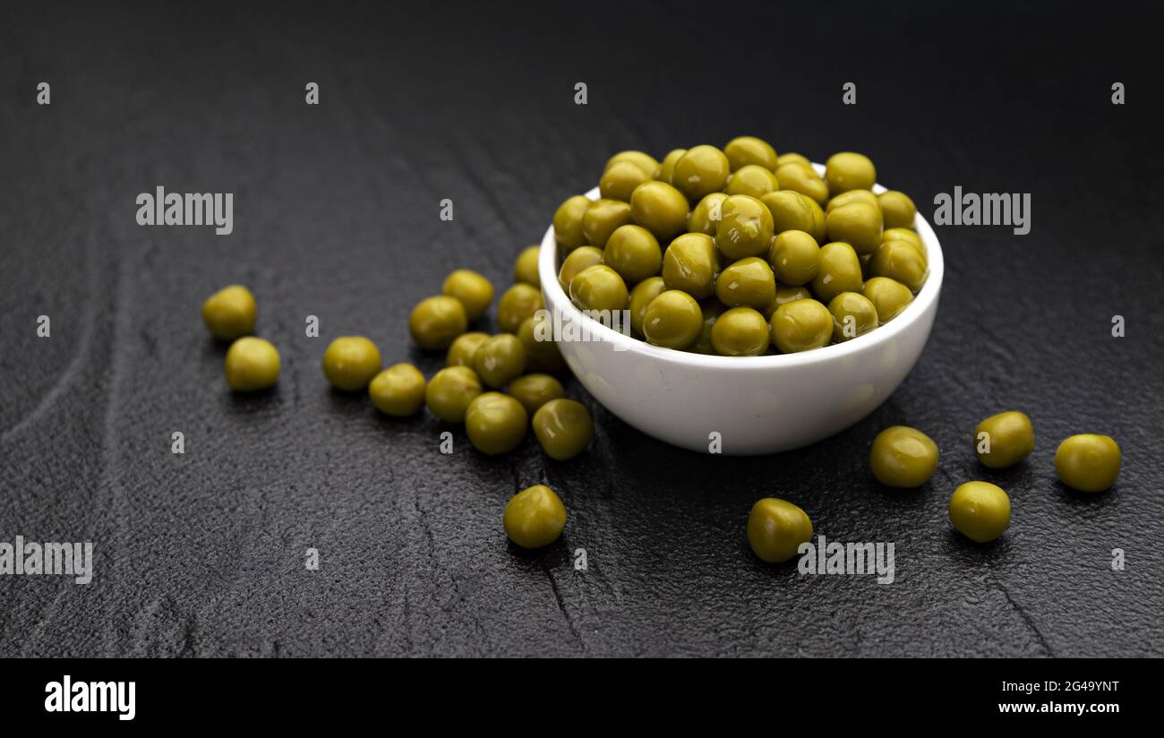 Mucchio di piselli verdi in scatola su sfondo nero Foto Stock
