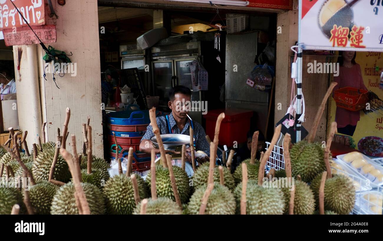 Cibo uomo che indossa camicia blu fumo sigaretta che vende frutta durian puzzolente è di fronte al suo negozio a Chinatown Bangkok Thailandia Foto Stock