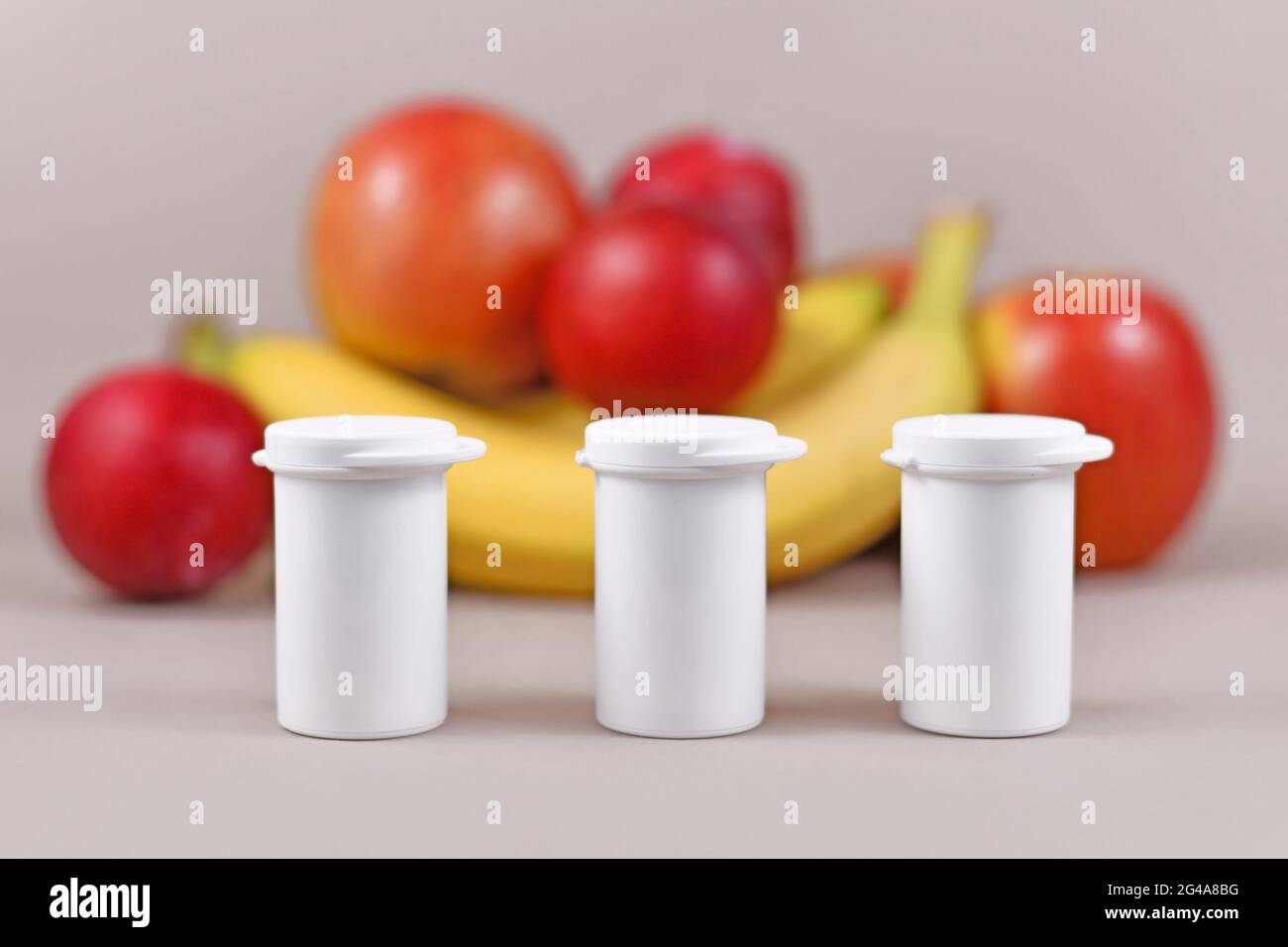 Piccole bottiglie con integratori alimentari di fronte a frutta e verdura su sfondo blu sfocato Foto Stock