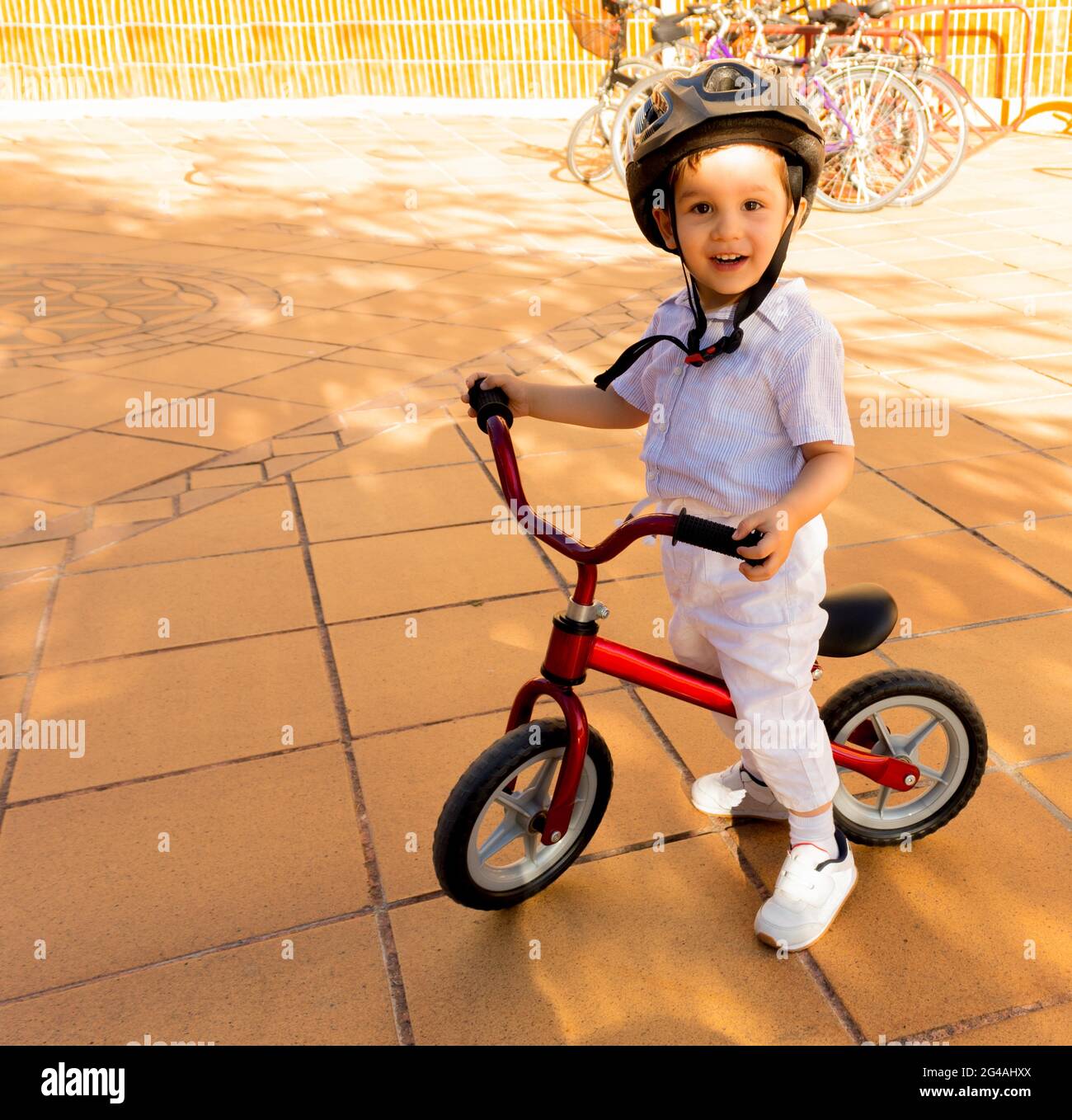 bambino sorridente e godendo di una bicicletta di apprendimento senza pedali con un casco protettivo in una giornata di sole Foto Stock