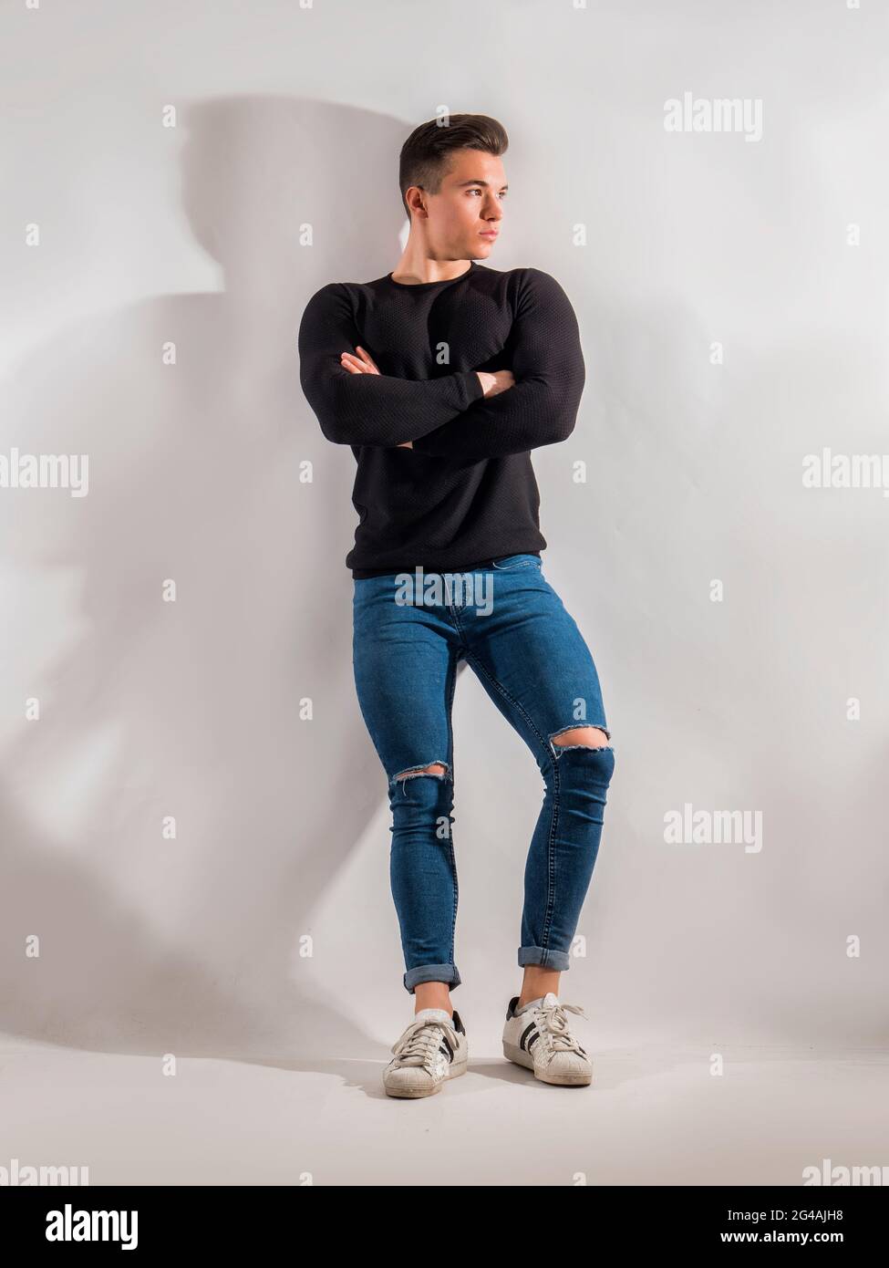 Un bel giovane in studio ha sparato, in piedi confindent con le braccia incrociate Foto Stock