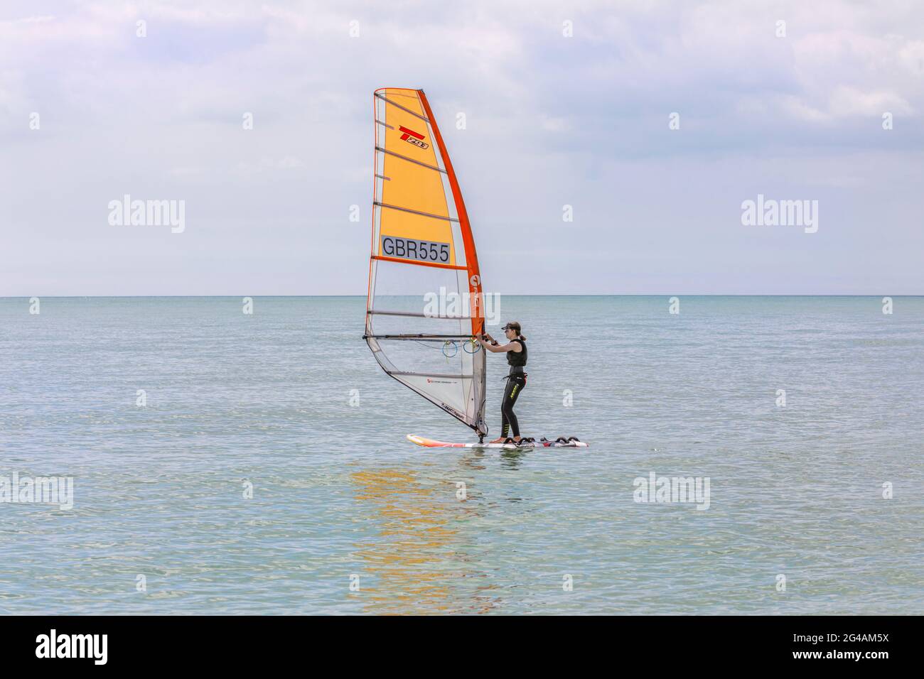 Una giovane donna che naviga sul vento su un mare calmo. Foto Stock