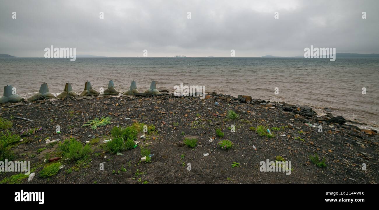 Bottiglie di plastica e altri rifiuti sulla riva del mare del Giappone vicino a Vladivostok. Giorno nuvoloso. Obiettivo grandangolare. Foto Stock