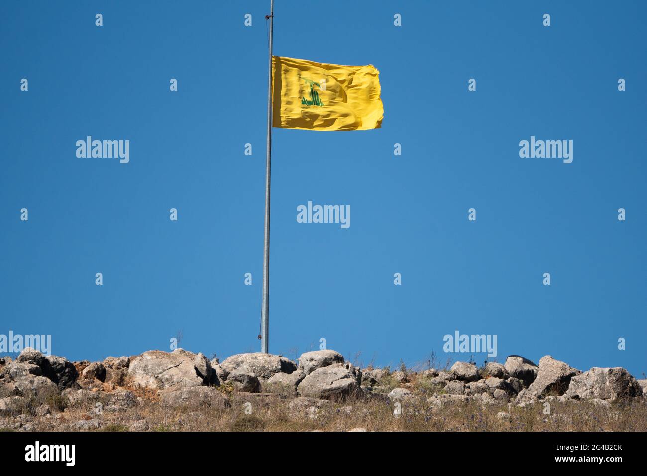 Bandiera gialla di Hezbollah con un cielo blu sullo sfondo del confine israeliano libanese Foto Stock