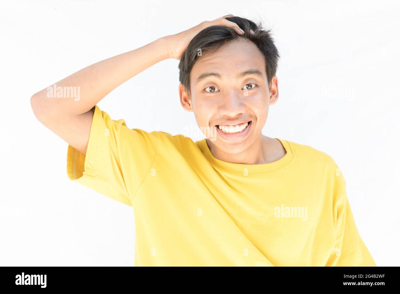 Un ragazzo indonesiano con una t-shirt gialla che guarda la macchina fotografica e sorride su uno sfondo bianco Foto Stock