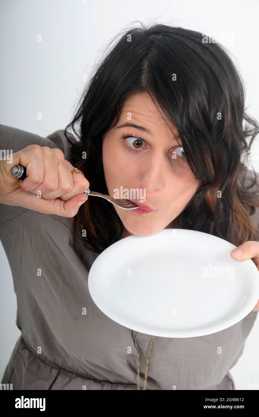 anoressia e disturbi alimentari concetto giovane donna mangia un singolo pisello su un grande studio di piastra bianca girato su sfondo bianco Foto Stock