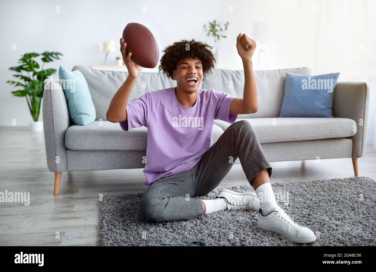 Eccitato teenager nero che guarda il calcio americano in televisione a casa, a tutta lunghezza Foto Stock