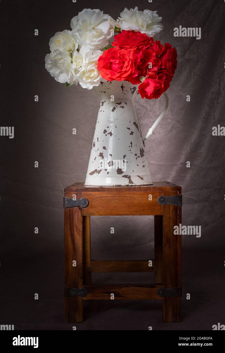 caraffa per latte vintage su un piccolo tavolo di legno contenente rose rosse e bianche in piena fioritura Foto Stock