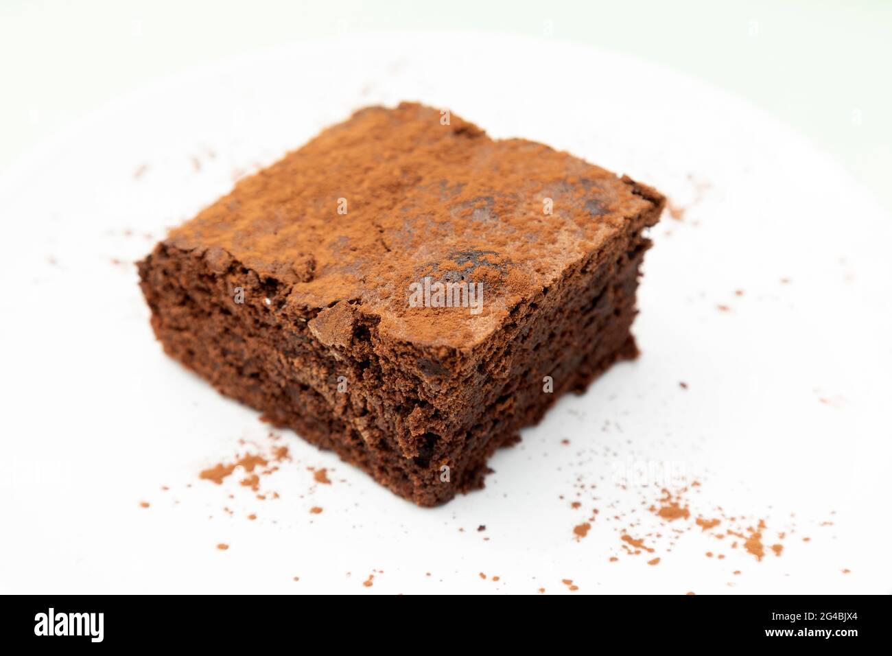 Brownie di cioccolato su un piatto di cacao-polvere. Il brownie è tagliato in un quadrato. Foto Stock