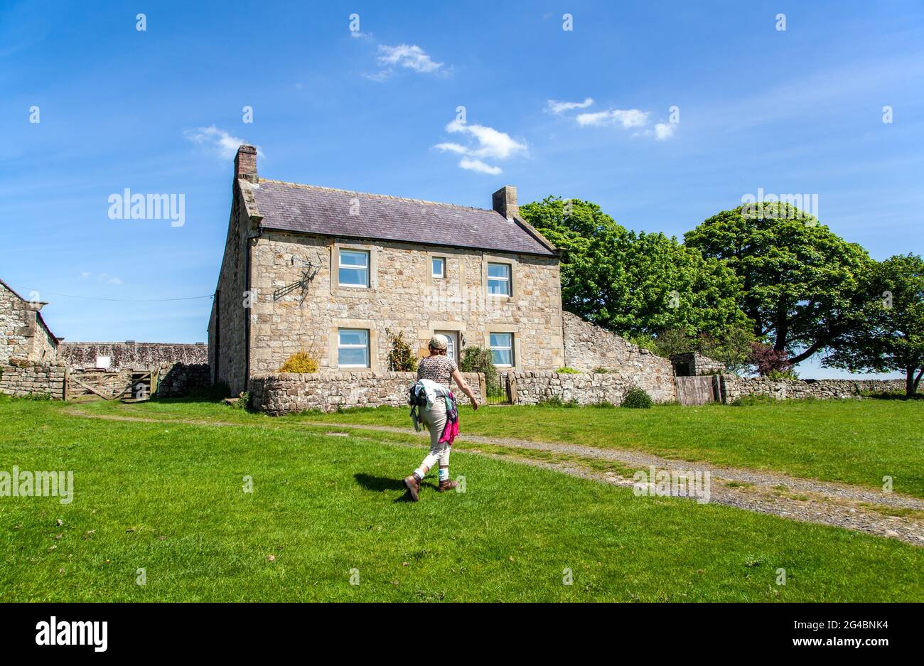 Donna che cammina attraverso la vecchia casa colonica mentre cammina Hadrians muro nazionale lunga distanza sentiero nel Northumberland Inghilterra Foto Stock