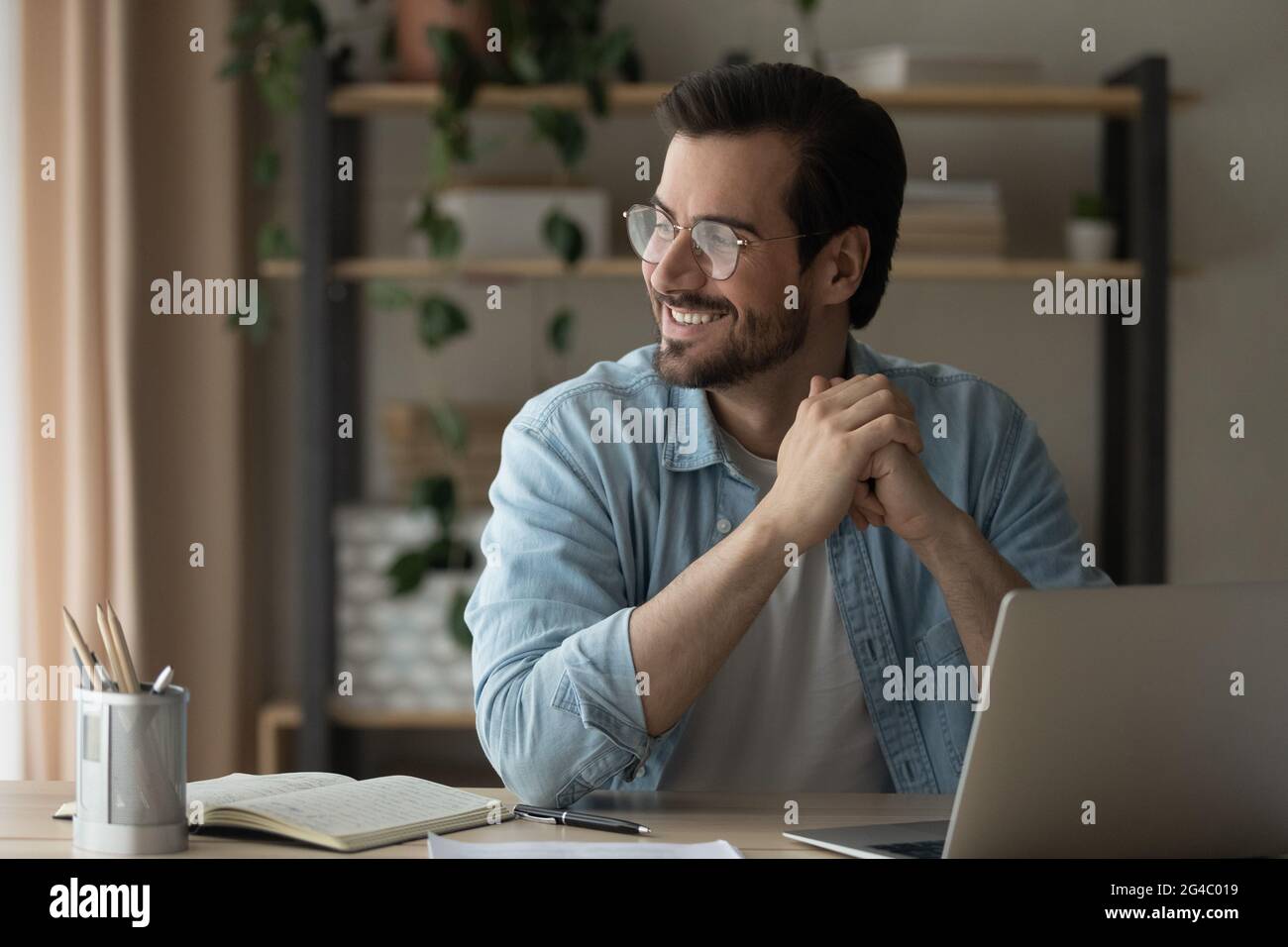 Sorridente giovane uomo in occhiali distratto dal lavoro al computer. Foto Stock