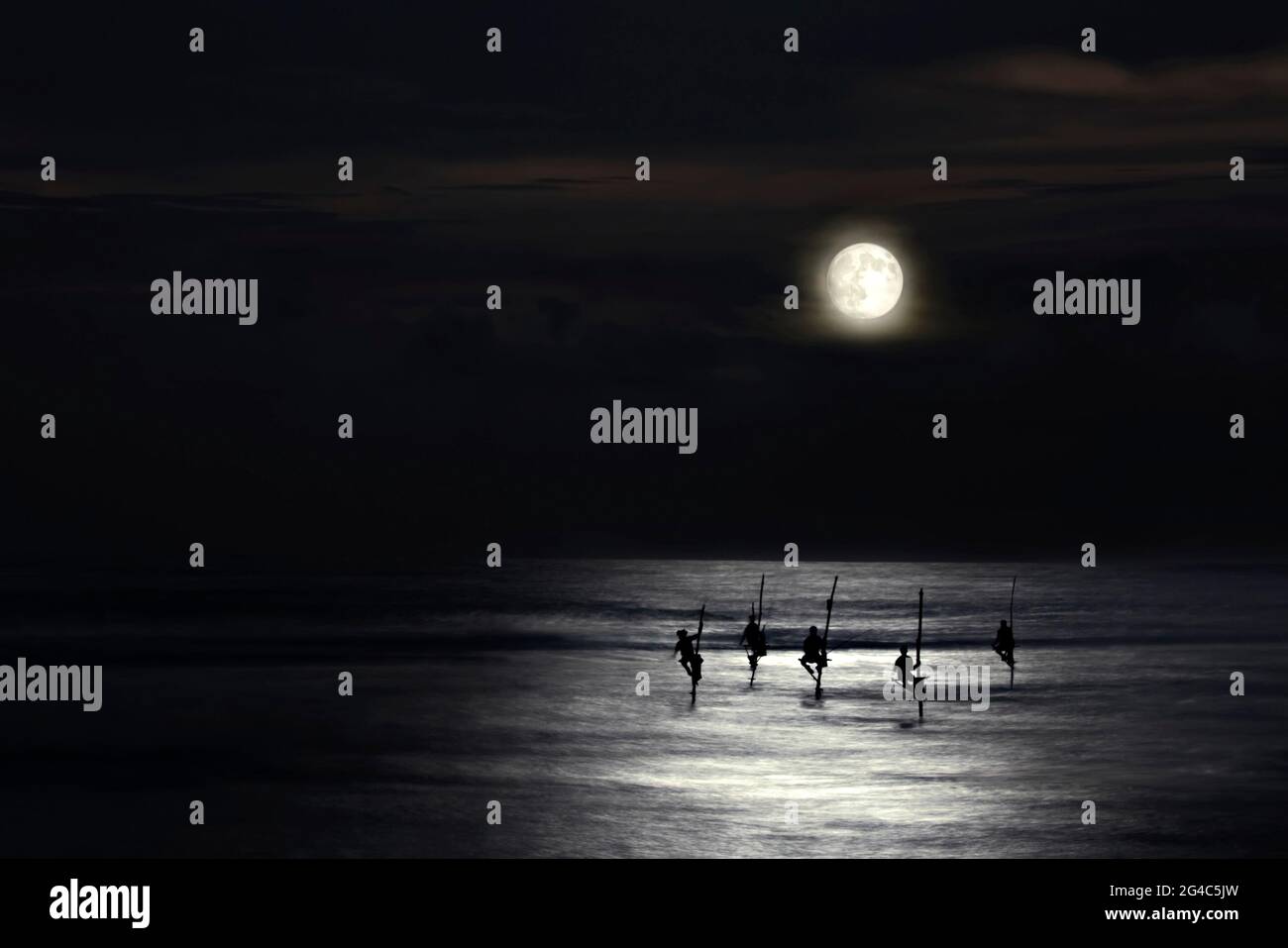 Pescatori su palafitte in silhouette al chiaro di luna a Galle, Sri Lanka Foto Stock