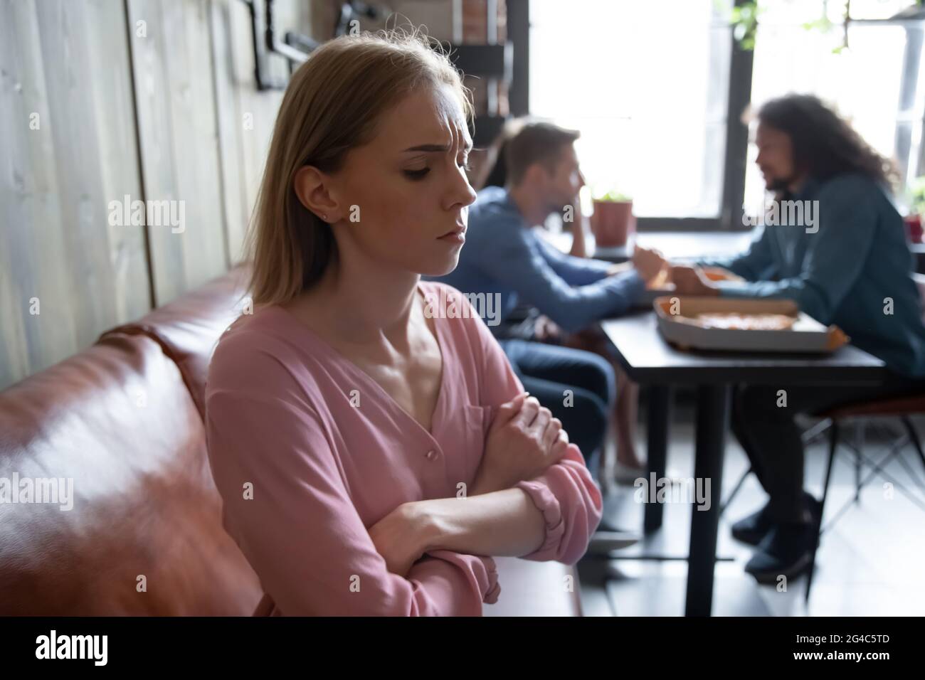 Giovane donna infelice, seduta separatamente dagli amici al bar. Foto Stock