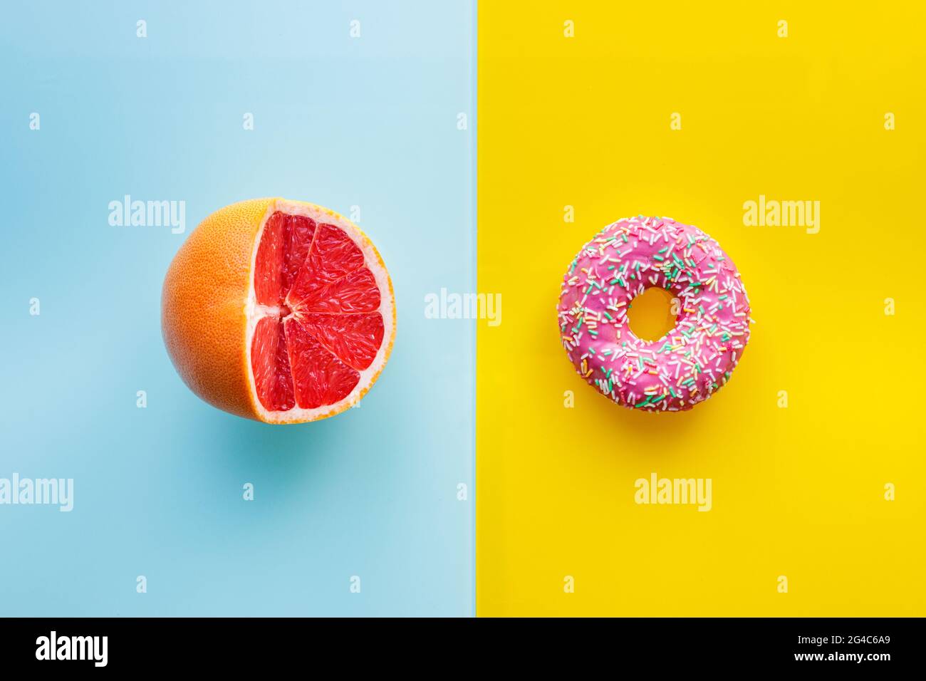 Cibo sano e malsano, strato piatto, sfondo a due colori, ciambelle rosa su giallo, pompelmo succoso su blu pastello, tagliato a metà Foto Stock