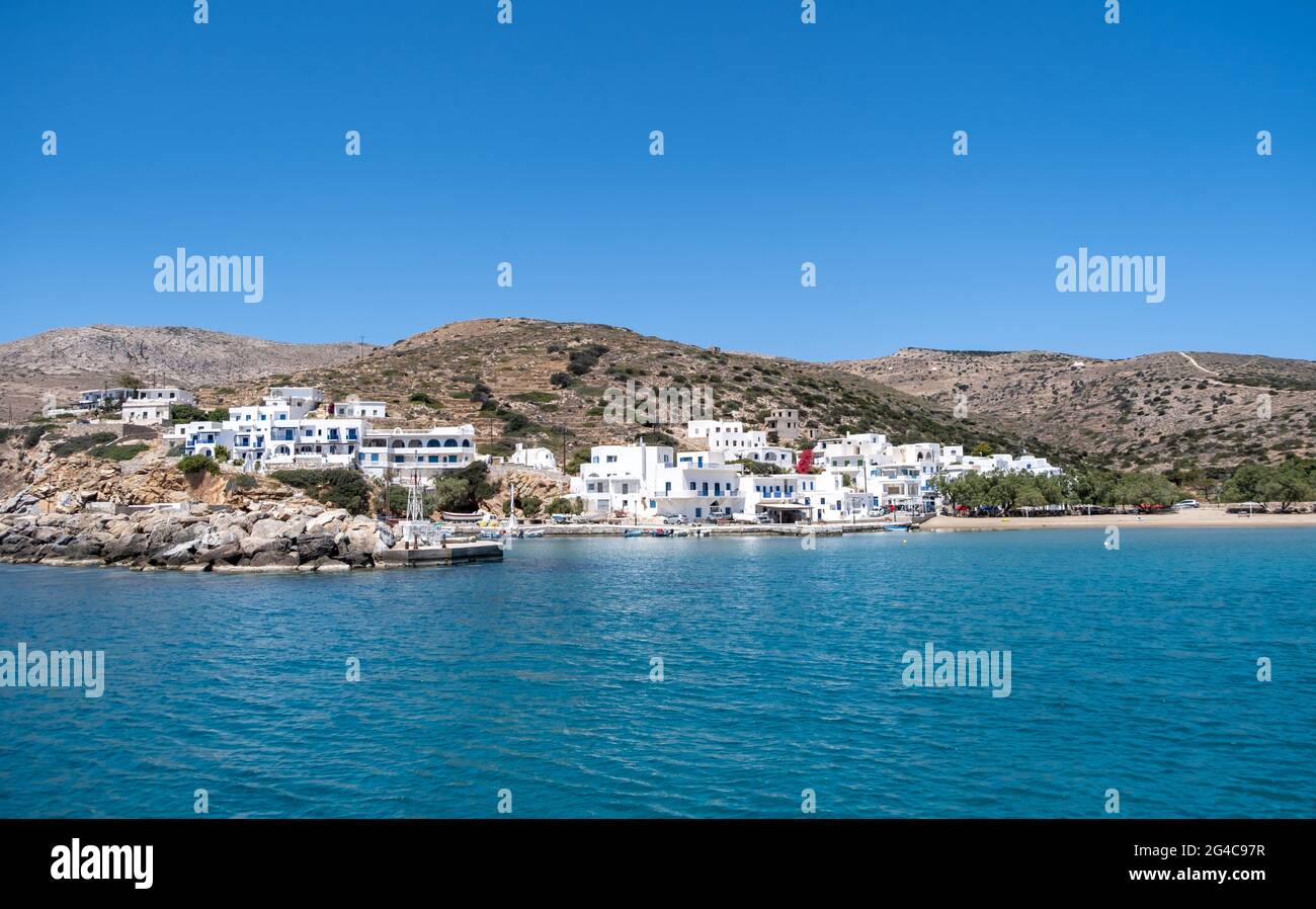 Porto dell'isola di Sikinos, edifici imbiancati e sfondo blu del cielo. Spiaggia di sabbia e acque turchesi limpide. Vacanze estive in una piccola isola greca, Cy Foto Stock