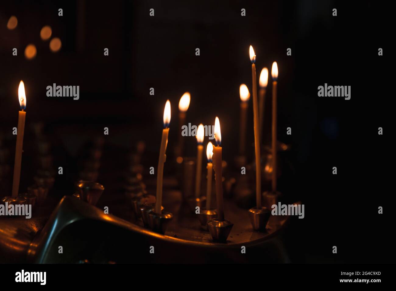 Piccole candele bruciano in una scura chiesa ortodossa, cristianesimo sfondo religioso Foto Stock