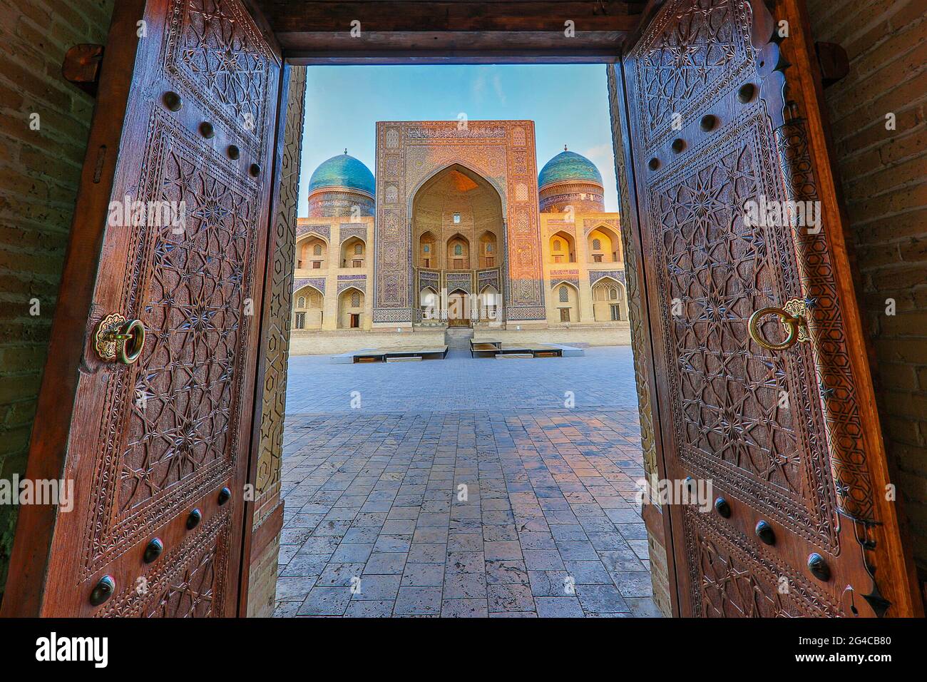 Vista sulla scuola teologica di poi Kalon, attraverso le porte in legno della moschea di Bukhara, Uzbekistan. Foto Stock